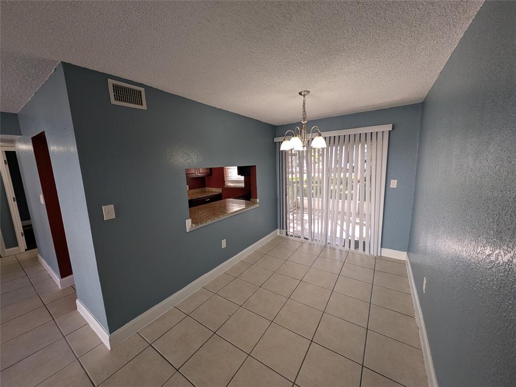 A dining area with blue walls, tile flooring, a chandelier, and a kitchen pass-through window — 2564 SE 15TH AVENUE UNIT E, OCALA, FL