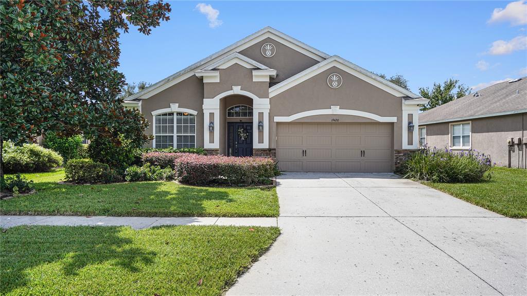 A single-story suburban house with a beige stucco exterior, a two-car garage, and landscaping — 19420 SUNSET BAY DRIVE, LAND O LAKES, FL