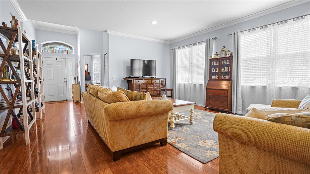 A living room features hardwood floors, a yellow sofa, a television console, and large windows — 19420 SUNSET BAY DRIVE, LAND O LAKES, FL