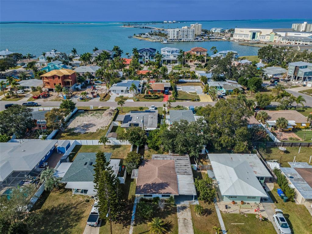 An aerial view shows a residential neighborhood with houses, palm trees, and a nearby bay — 2476 CORONADO WAY, DUNEDIN, FL