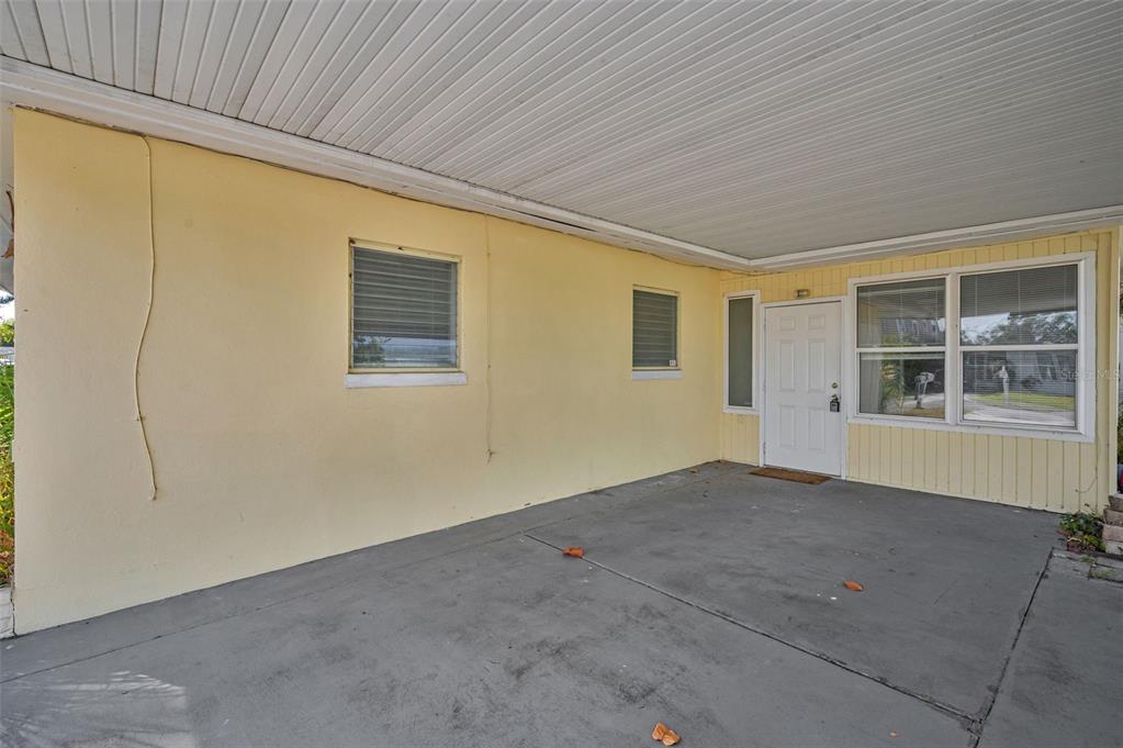 A concrete carport with a yellow exterior wall, two windows, and a white front door — 2476 CORONADO WAY, DUNEDIN, FL