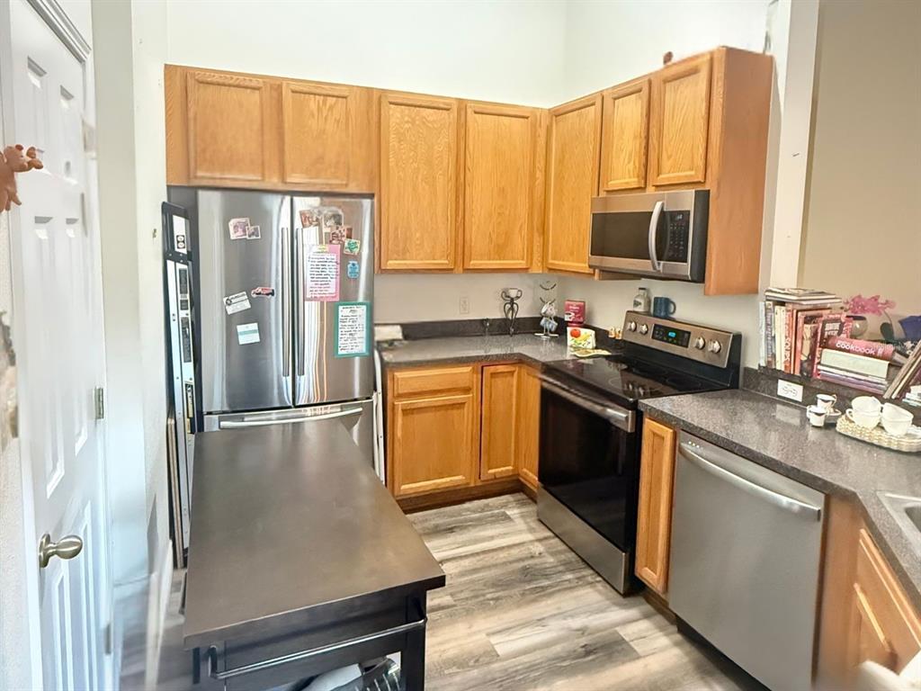 A kitchen features wood cabinets, stainless steel appliances, and dark countertops over wood-look flooring — 8621 SHALLOW CREEK COURT, NEW PORT RICHEY, FL