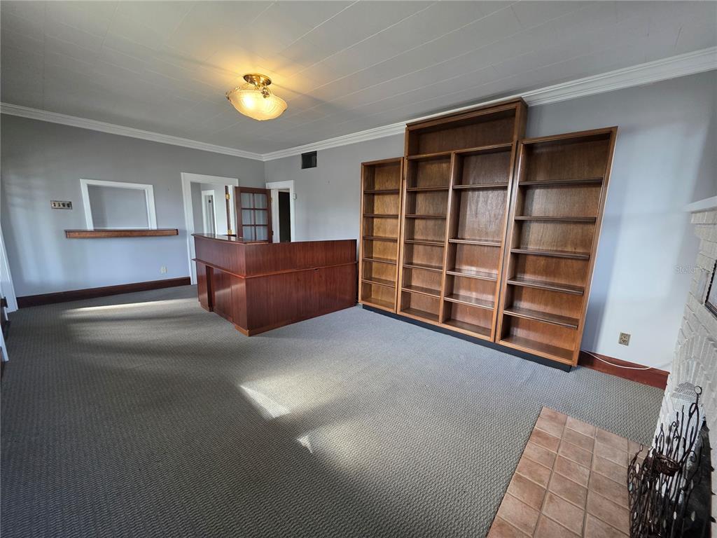 A room with gray carpet, a wooden bar, built-in bookshelves, and a brick fireplace — 1700 S WASHINGTON AVENUE, TITUSVILLE, FL