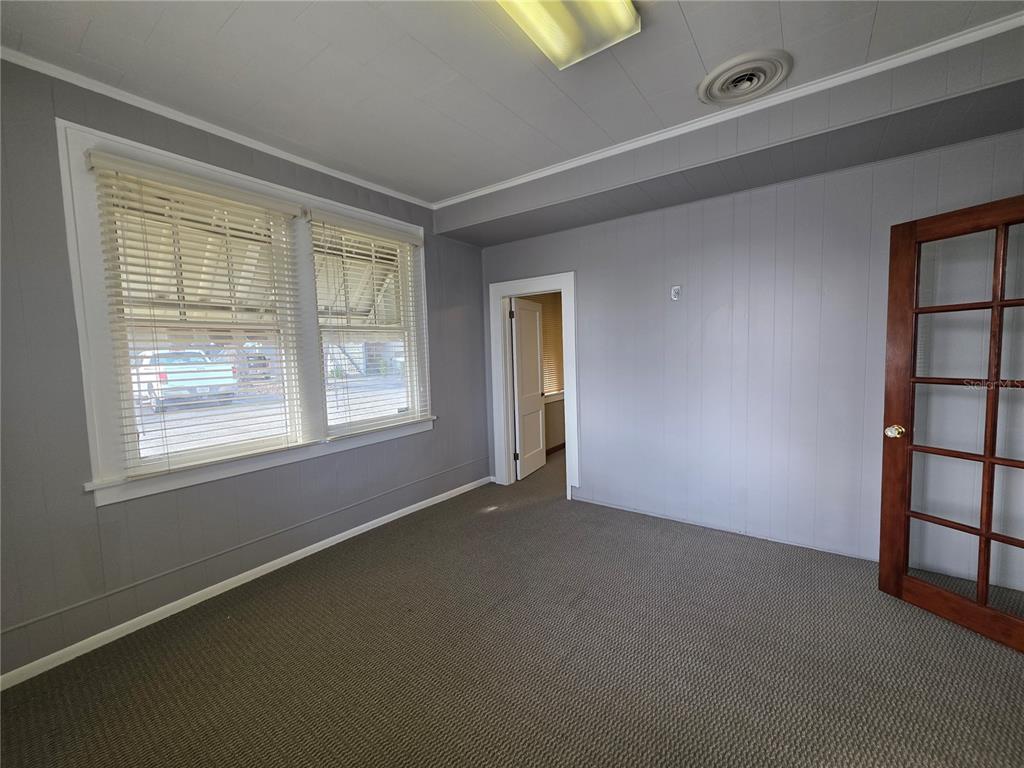 An empty room features gray paneled walls, gray carpeting, a window with blinds, and a door — 1700 S WASHINGTON AVENUE, TITUSVILLE, FL