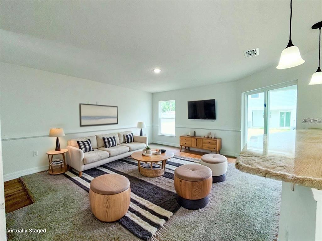 This virtually staged living room features a sofa, coffee table, ottomans, and a television — 222 CARPENTERS WAY UNIT 66, LAKELAND, FL