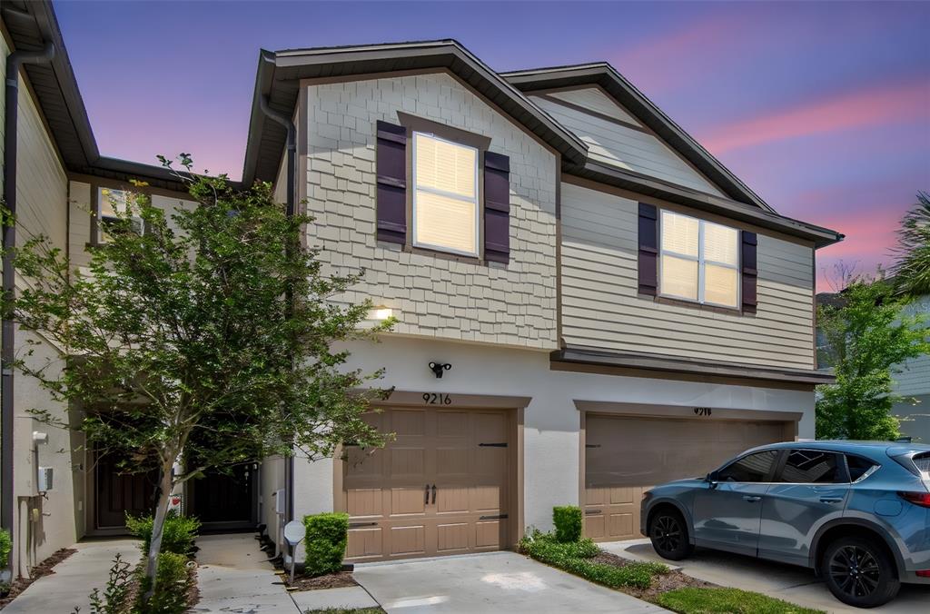 A two-story townhouse exterior with tan siding, shake shingles, and two attached garages — 9216 HILLCROFT DRIVE, RIVERVIEW, FL