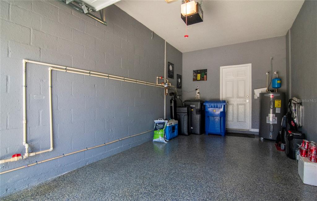 A garage with gray painted block walls, epoxy flooring, a water heater, and plumbing pipes — 9216 HILLCROFT DRIVE, RIVERVIEW, FL