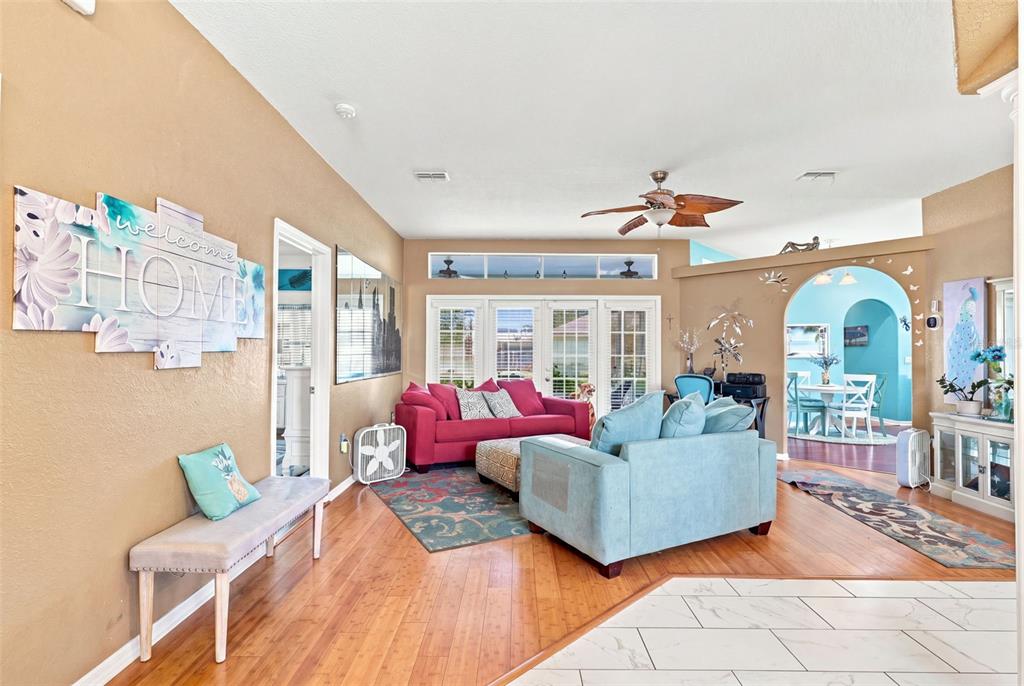 A living room features hardwood floors, a red sofa, a blue armchair, and a dining area — 13476 LITTLE FARMS DRIVE, SPRING HILL, FL