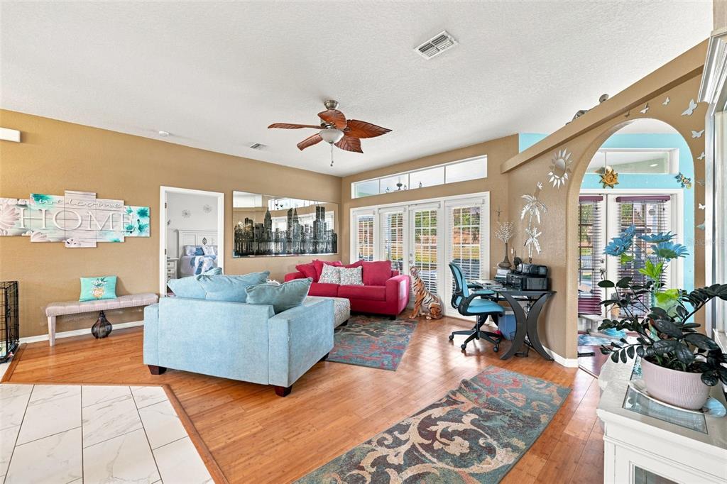 A living room features hardwood floors, a ceiling fan, a blue sofa, and a red sofa — 13476 LITTLE FARMS DRIVE, SPRING HILL, FL