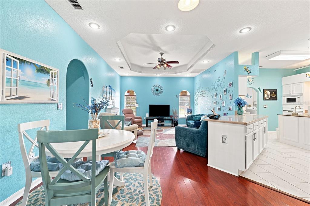 An open-concept living and dining area features bright blue walls, hardwood floors, and white cabinetry — 13476 LITTLE FARMS DRIVE, SPRING HILL, FL