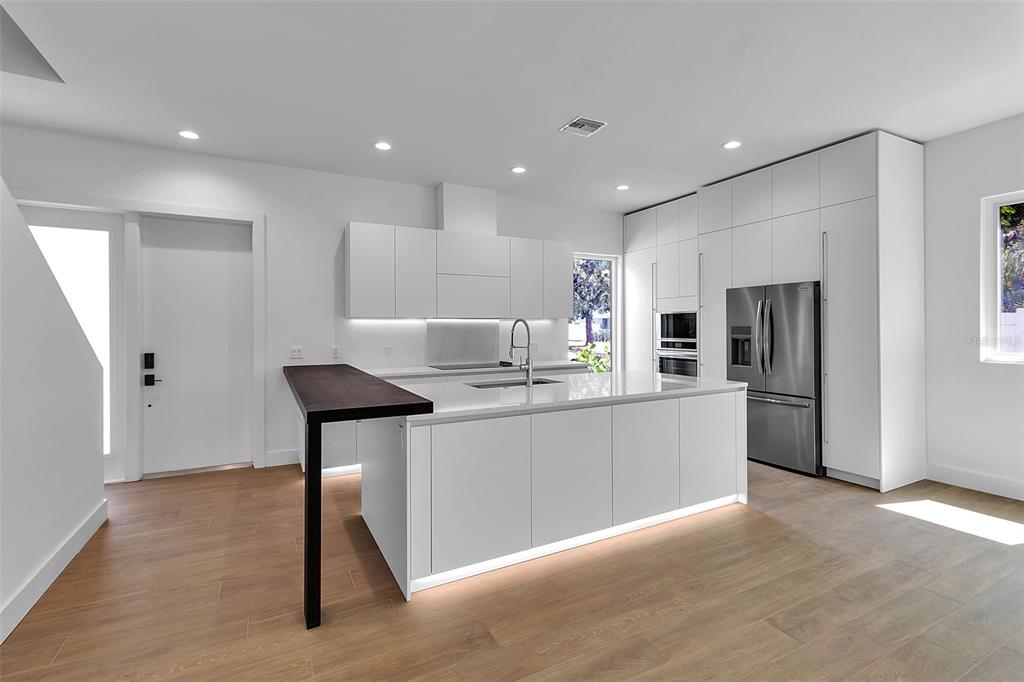 A modern kitchen features white cabinetry, marble countertops, and a dark wood breakfast bar — 2516 BROWNING STREET, SARASOTA, FL