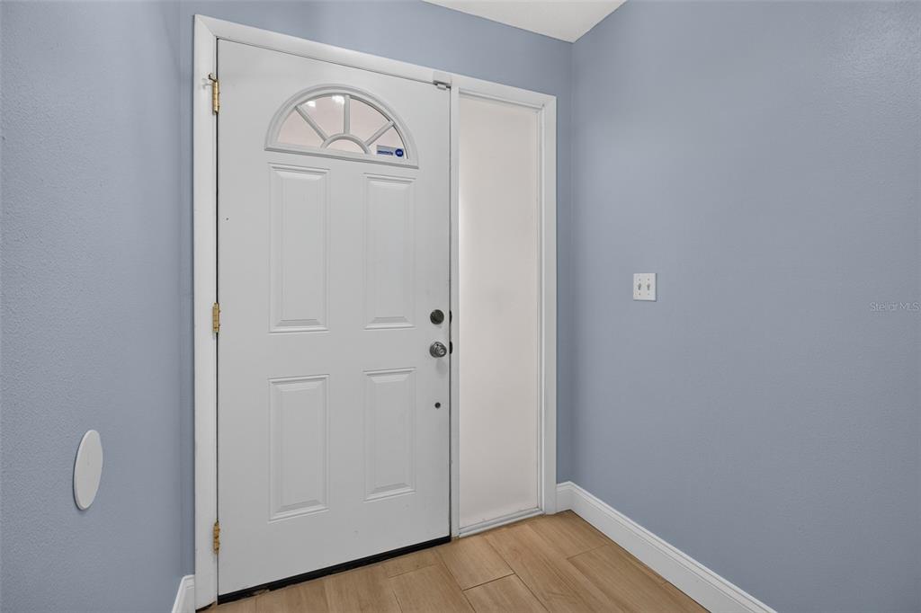 A white front door with a sidelight opens into an entryway with light wood flooring — 12499 82ND TERRACE, SEMINOLE, FL