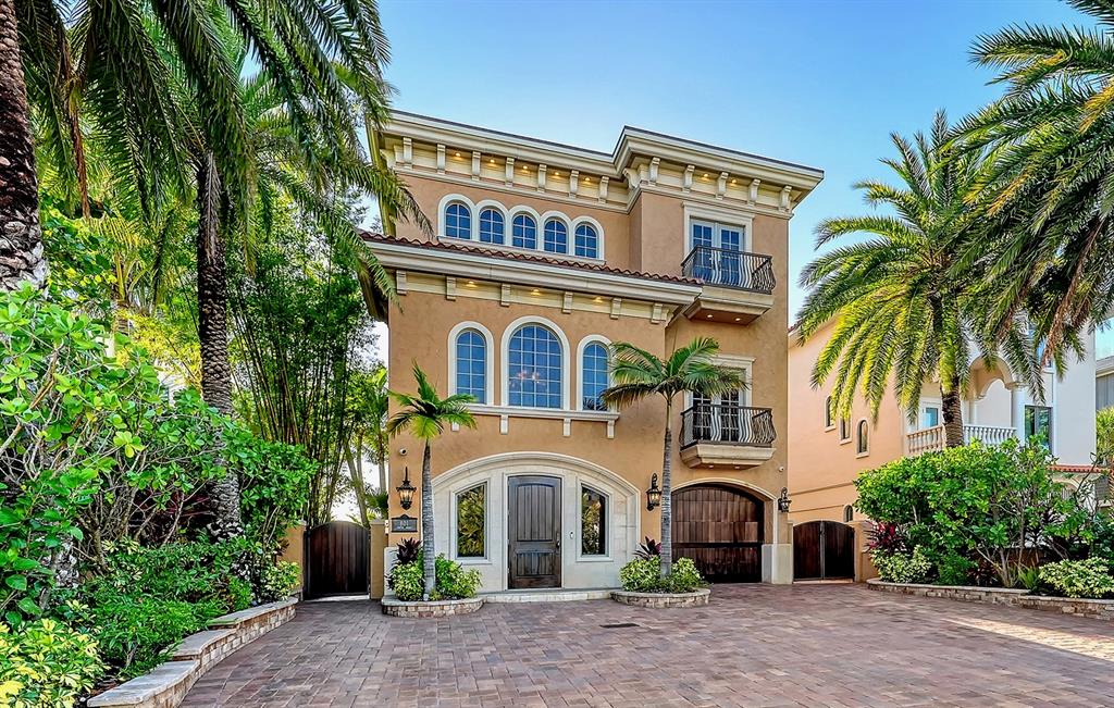 A three-story tan stucco house with a dark wood garage door and palm trees — 801 N SHORE DRIVE, ANNA MARIA, FL