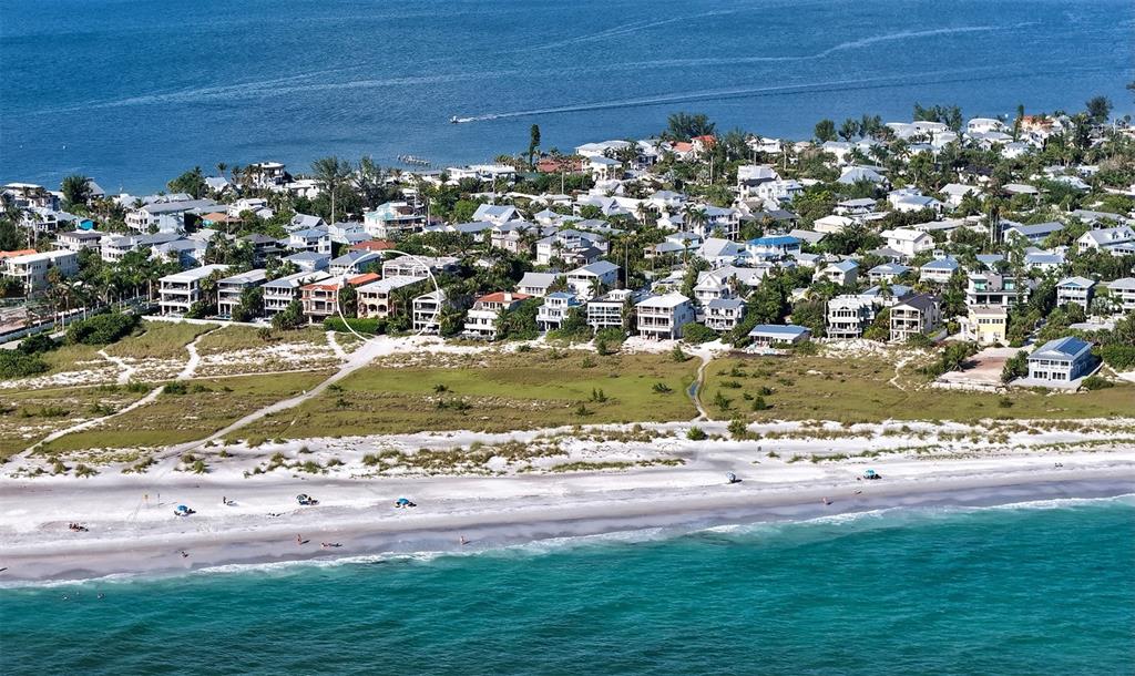 An aerial view shows a multi-story house circled on a beach with nearby coastal homes — 801 N SHORE DRIVE, ANNA MARIA, FL