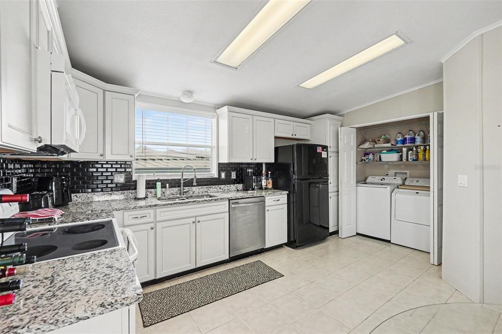 A kitchen with white cabinets, granite countertops, black subway tile backsplash, and an adjacent laundry closet — 226 BIMINI DRIVE, PALMETTO, FL