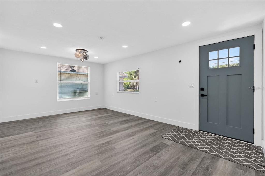 A bright living room features white walls, gray wood-look flooring, recessed lighting, and a door — 246 WILLOW PLACE, ORMOND BEACH, FL