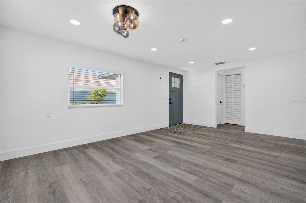 A bright, empty room features gray wood-look flooring, white walls, a dark door, and recessed lighting — 246 WILLOW PLACE, ORMOND BEACH, FL