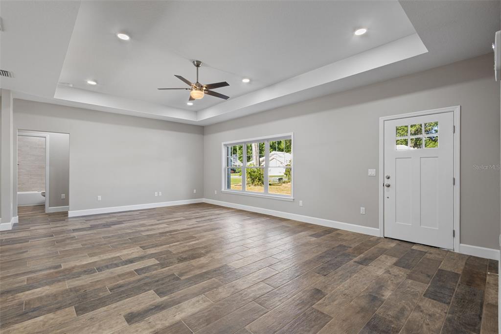 A spacious living room features light gray walls, wood-look tile flooring, and a tray ceiling — 9100 DORIE DRIVE, TRENTON, FL