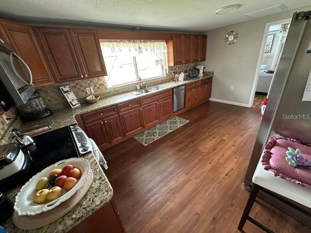 A kitchen features wood cabinets, granite countertops, stainless steel appliances, and wood-look flooring — 1509 TATE STREET, COCOA, FL