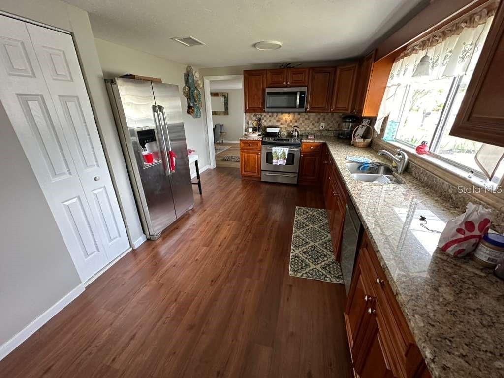 A kitchen features wood-look flooring, stainless steel appliances, granite countertops, and dark wood cabinetry — 1509 TATE STREET, COCOA, FL