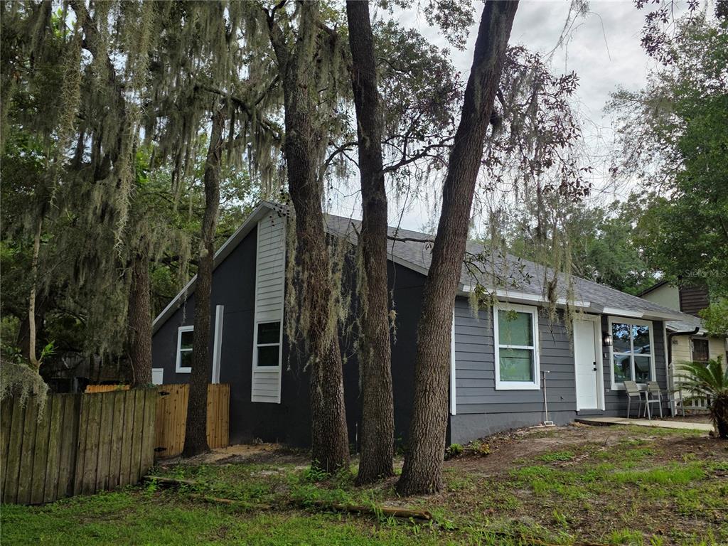 A dark gray single-story house with white trim stands among trees draped in Spanish moss — 1422 PLYMOUTH AVENUE, MOUNT DORA, FL