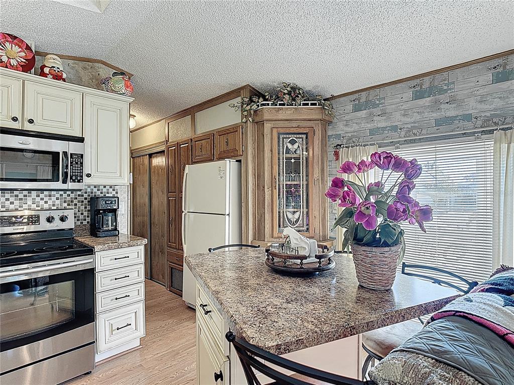 A kitchen features white cabinets, stainless steel appliances, a granite island, and wood-look wall paneling — 9000 US HWY 192 UNIT 214, CLERMONT, FL