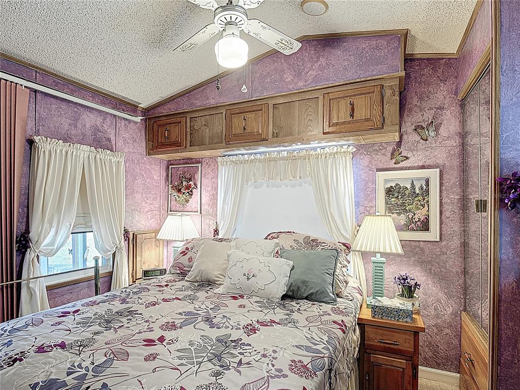 A bedroom features a bed with floral bedding, purple textured walls, and overhead wooden cabinets — 9000 US HWY 192 UNIT 214, CLERMONT, FL