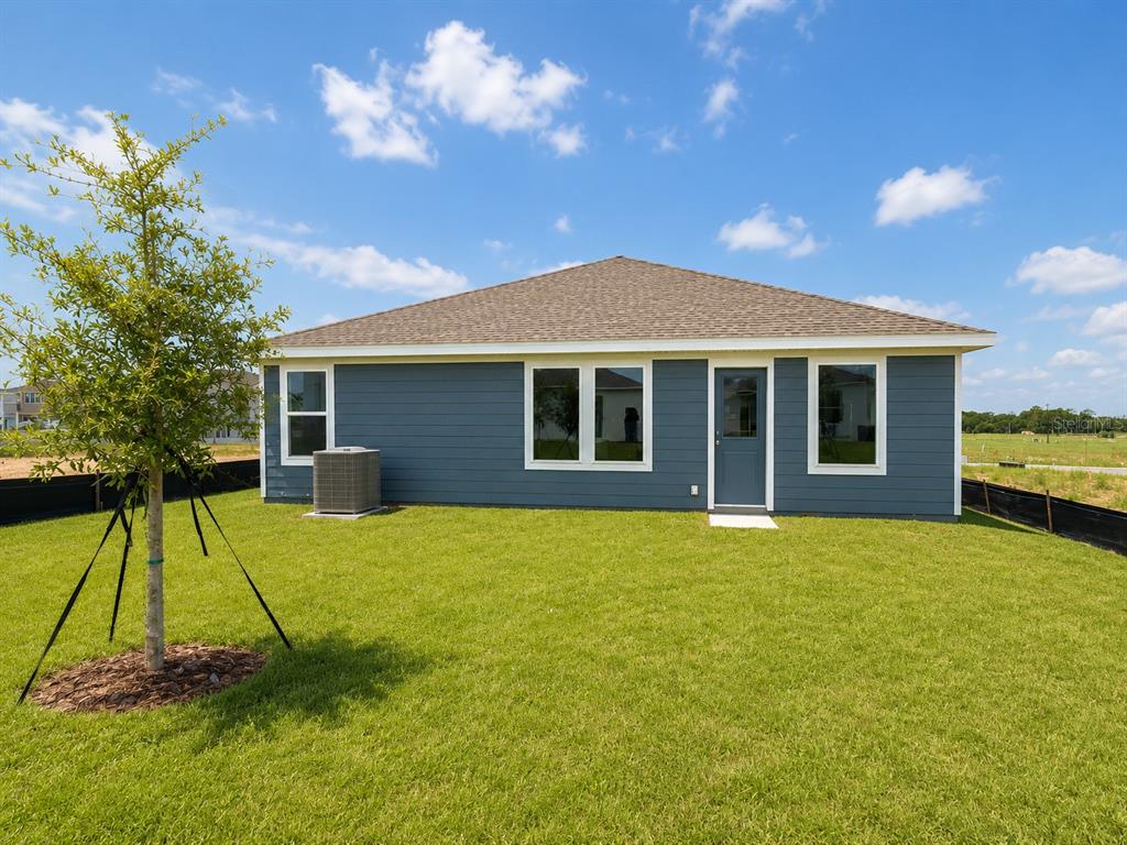 The rear exterior of a blue single-story house features a lawn, tree, and AC unit — 3171 TOTEM ROAD, EAGLE LAKE, FL