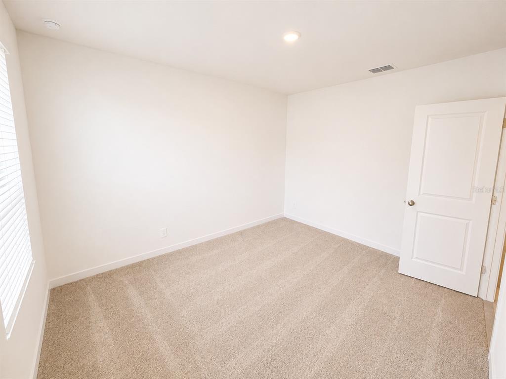An empty bedroom features beige carpet, white walls, a window with blinds, and a closed door — 3171 TOTEM ROAD, EAGLE LAKE, FL
