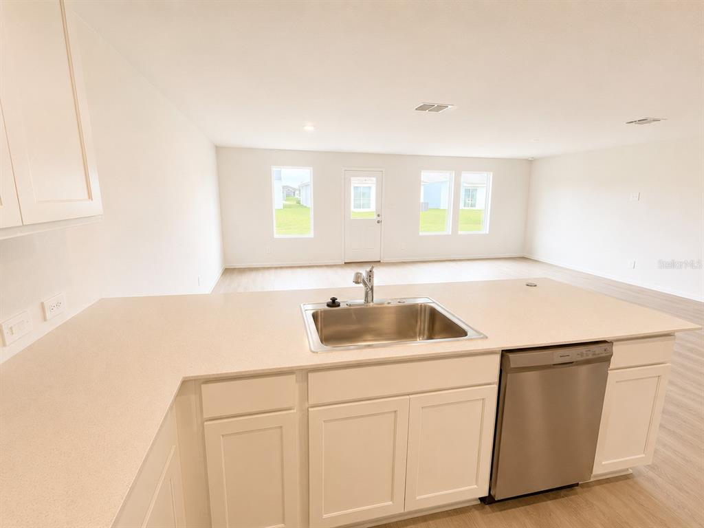 A kitchen with white cabinets, a stainless steel sink, and a dishwasher overlooks a living area — 3171 TOTEM ROAD, EAGLE LAKE, FL