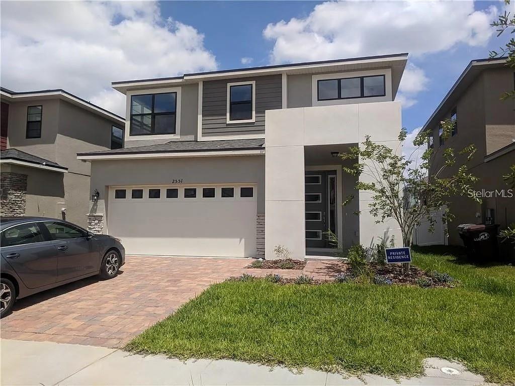 A two-story house with a paved driveway, a two-car garage, and a modern white entryway — 2551 AVIAN LOOP, KISSIMMEE, FL