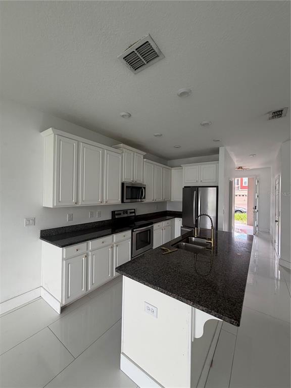 A kitchen features white cabinets, dark granite countertops, stainless steel appliances, and white tile flooring — 2551 AVIAN LOOP, KISSIMMEE, FL