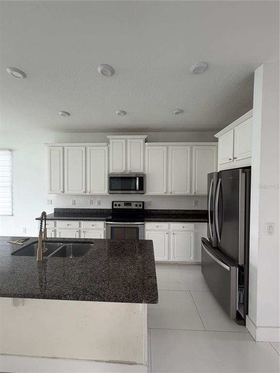 A kitchen features white cabinets, dark granite countertops, stainless steel appliances, and white tile flooring — 2551 AVIAN LOOP, KISSIMMEE, FL