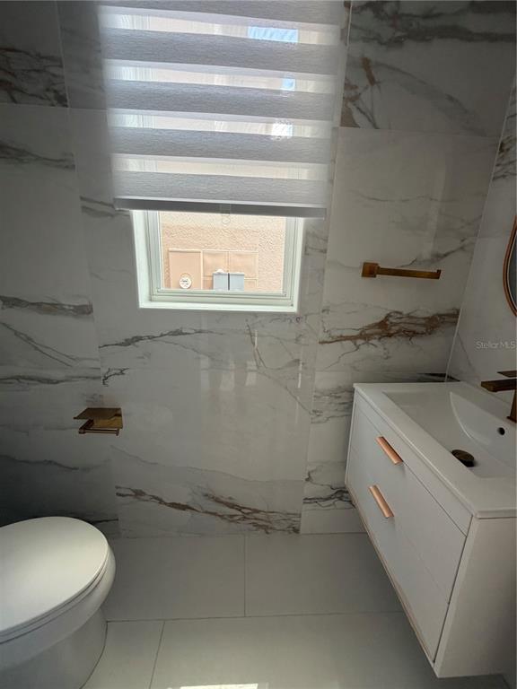 A bathroom features white marble-look wall tiles, a floating vanity, and a window with blinds — 2551 AVIAN LOOP, KISSIMMEE, FL