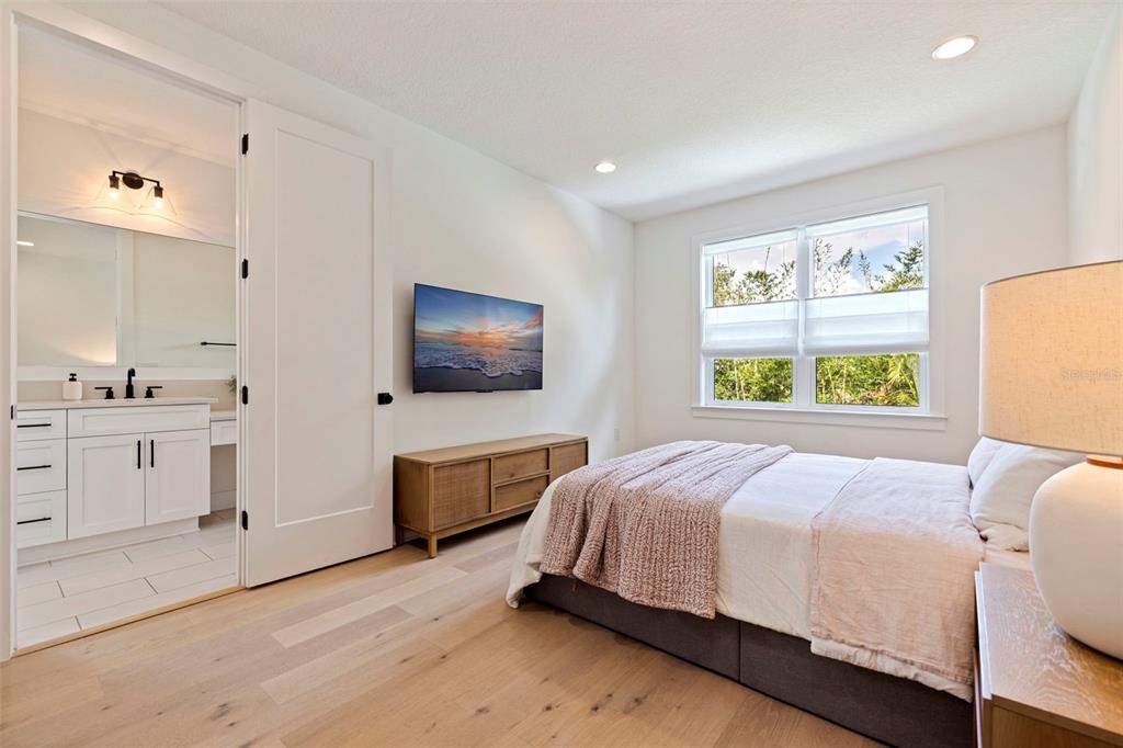 A bedroom with light wood floors, a bed, a wall-mounted television, and an attached bathroom — 410 S HABANA AVENUE UNIT 1, TAMPA, FL