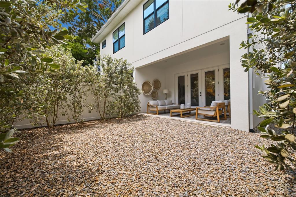 A gravel backyard features a covered patio with outdoor seating and white exterior walls — 410 S HABANA AVENUE UNIT 1, TAMPA, FL