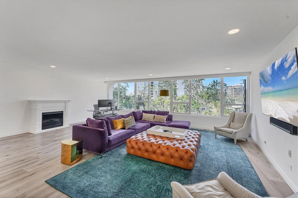 A living room features a purple sectional sofa, a leather ottoman, and large floor-to-ceiling windows — 100 SANDS POINT ROAD UNIT 323, LONGBOAT KEY, FL