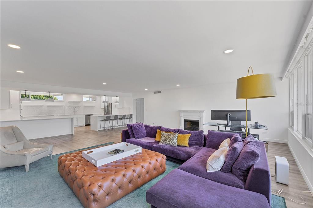 A bright open-concept living room features a purple sectional sofa, leather ottoman, and white kitchen — 100 SANDS POINT ROAD UNIT 323, LONGBOAT KEY, FL