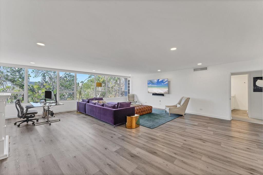 A spacious living room features light wood-look flooring, a purple sectional sofa, and floor-to-ceiling windows — 100 SANDS POINT ROAD UNIT 323, LONGBOAT KEY, FL