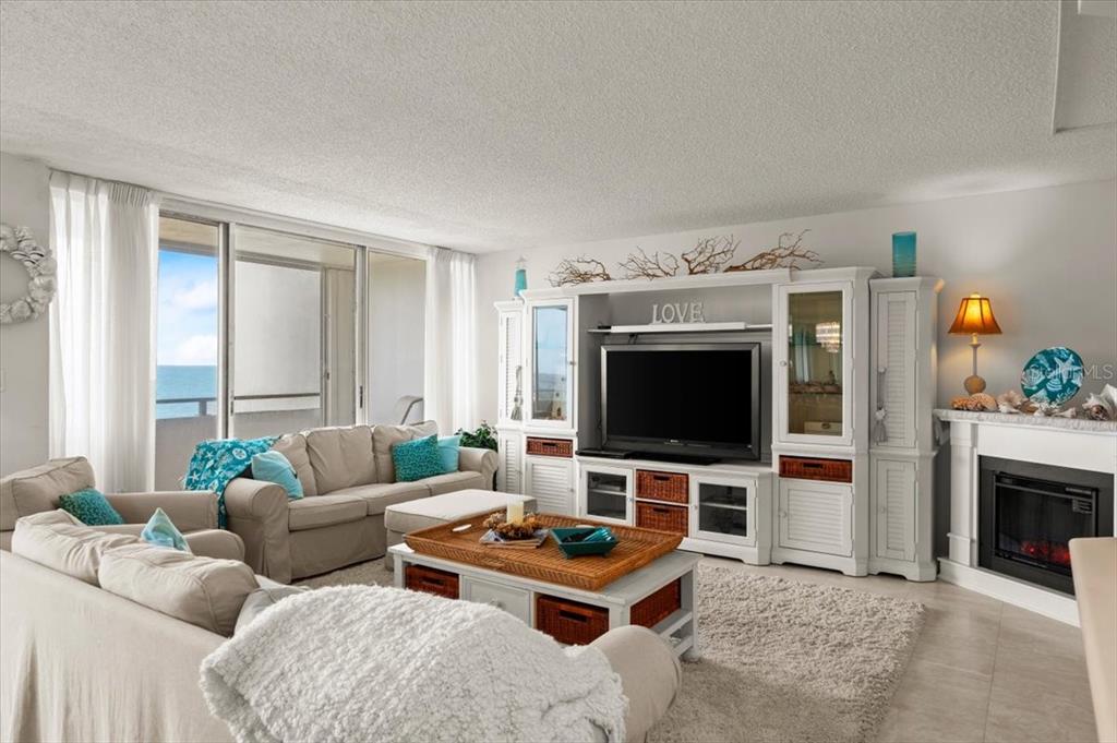 A living room features a beige sofa, a television console, and a fireplace near windows — 901 S ATLANTIC AVENUE UNIT PH3, ORMOND BEACH, FL