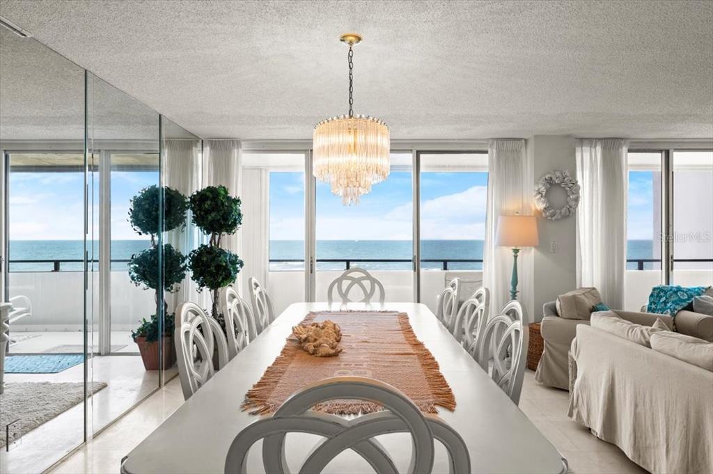 A dining room features a crystal chandelier, white chairs, and a view of the ocean — 901 S ATLANTIC AVENUE UNIT PH3, ORMOND BEACH, FL