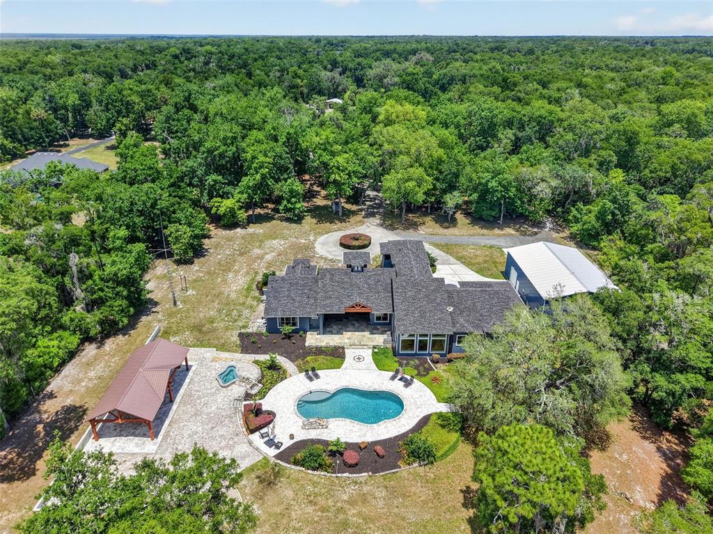 An aerial view shows a house with a pool, patio, and detached garage in woods — 2110 HIGHLAND PARK ROAD, DELAND, FL