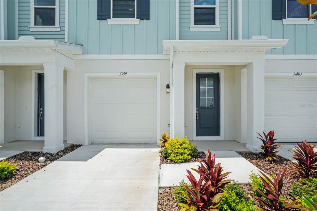 The exterior of a two-story townhouse features a garage, a front door, and landscaping — 31799 KESTREL CALLING DRIVE, SAN ANTONIO, FL