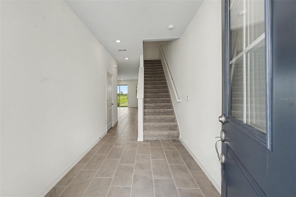 An entryway with gray tile flooring leads to a carpeted staircase and a rear doorway — 31799 KESTREL CALLING DRIVE, SAN ANTONIO, FL