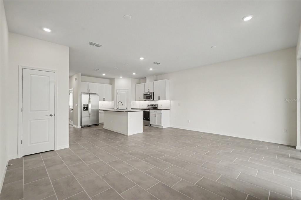 An open-concept kitchen with white cabinets, stainless steel appliances, and gray tile flooring — 31799 KESTREL CALLING DRIVE, SAN ANTONIO, FL