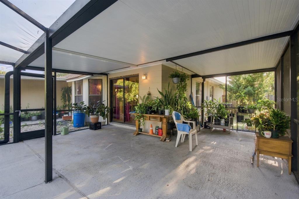 A screened-in patio features a concrete floor, a covered roof, and numerous potted plants — 207 LIMONA ROAD, BRANDON, FL