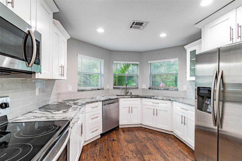A kitchen with white cabinets, stainless steel appliances, granite countertops, and wood-look flooring — 3208 W NAPOLEON AVENUE, TAMPA, FL