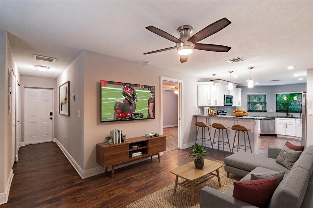 A living room with wood floors, a wall-mounted television, and an open kitchen with bar seating — 3208 W NAPOLEON AVENUE, TAMPA, FL