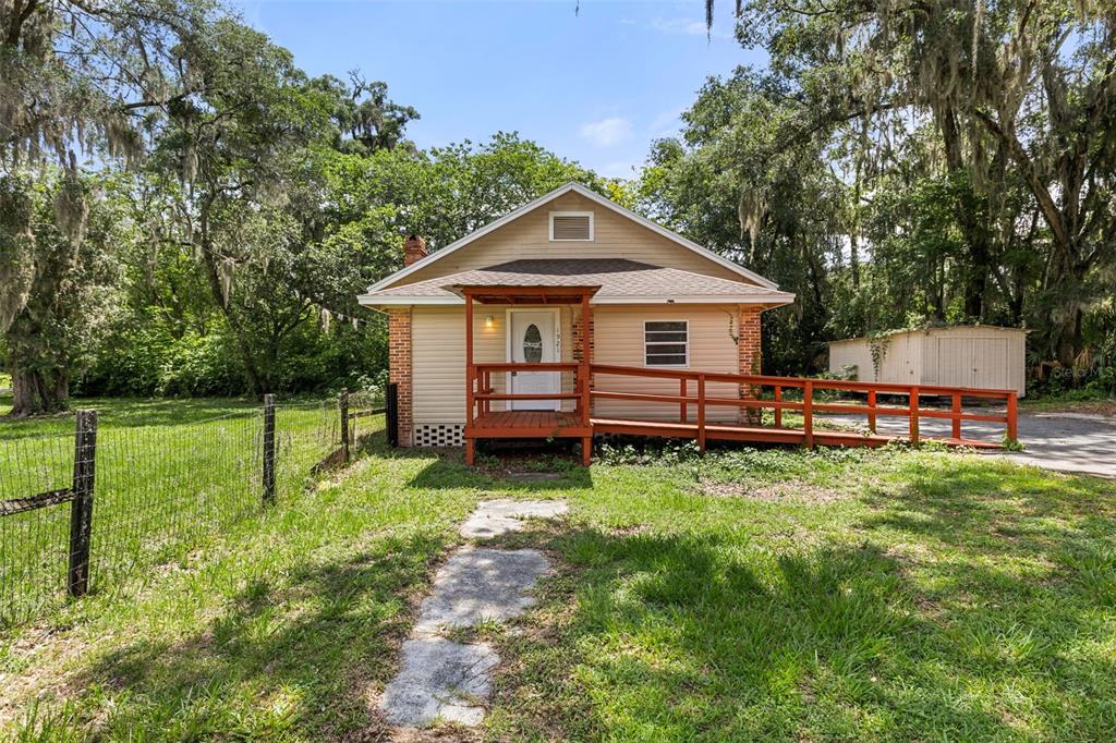 A single-story house with tan siding, a brick chimney, and a wooden wheelchair ramp — 1921 NE 8TH ROAD, OCALA, FL