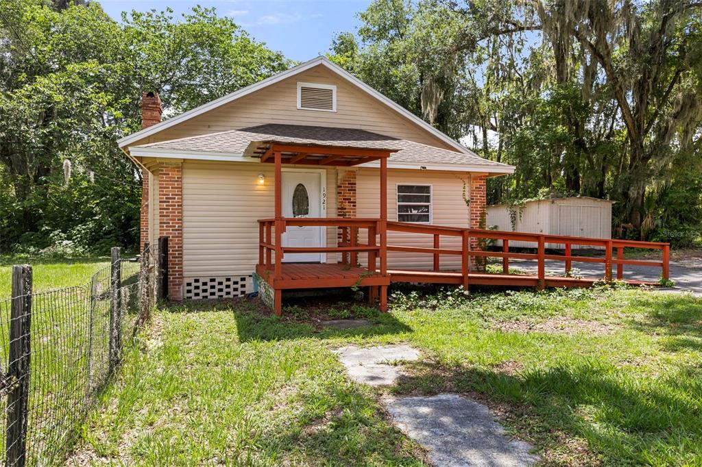 A small, beige, single-story house with a brick chimney and a wooden wheelchair ramp — 1921 NE 8TH ROAD, OCALA, FL